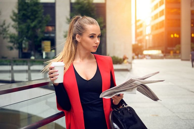 mulher elegante de pé ao ar livre com uma chávena e jornais
