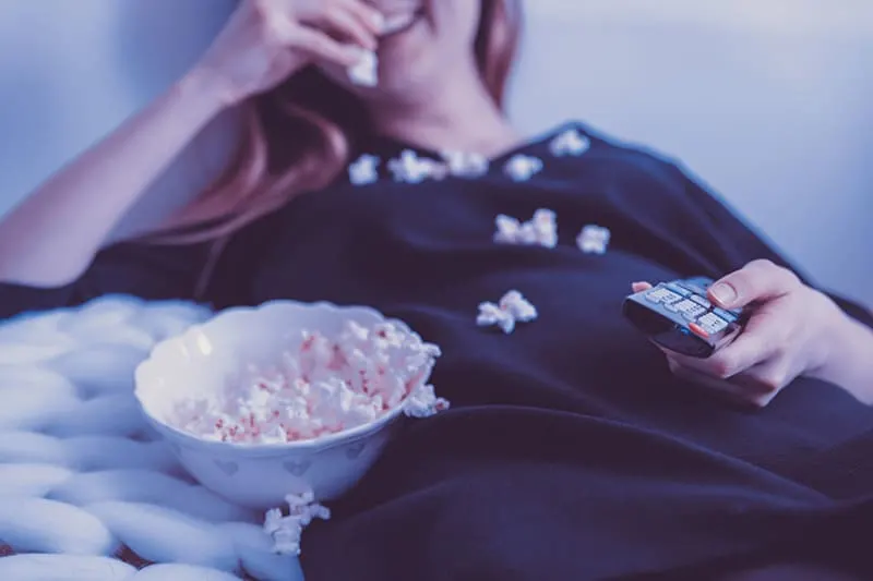 Woman lying on bed while earting popcorn