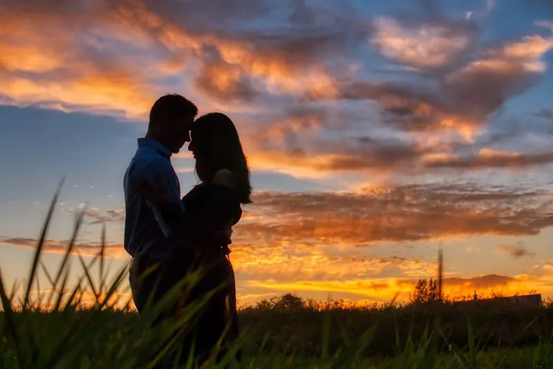 a hugging couple in the field on the sunset