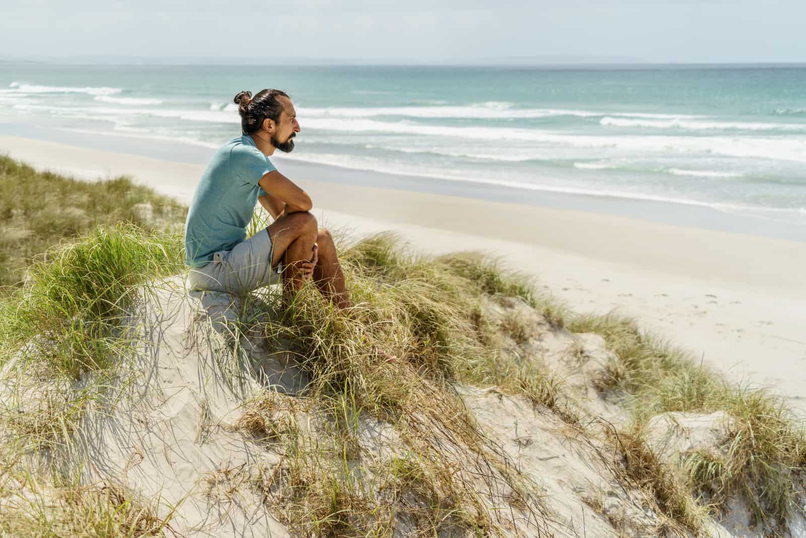 um homem senta-se na areia e olha para o mar