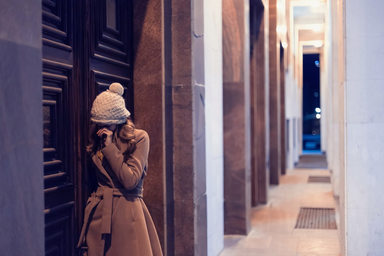 a sad girl in a brown coat stands in the hallway in front of the door