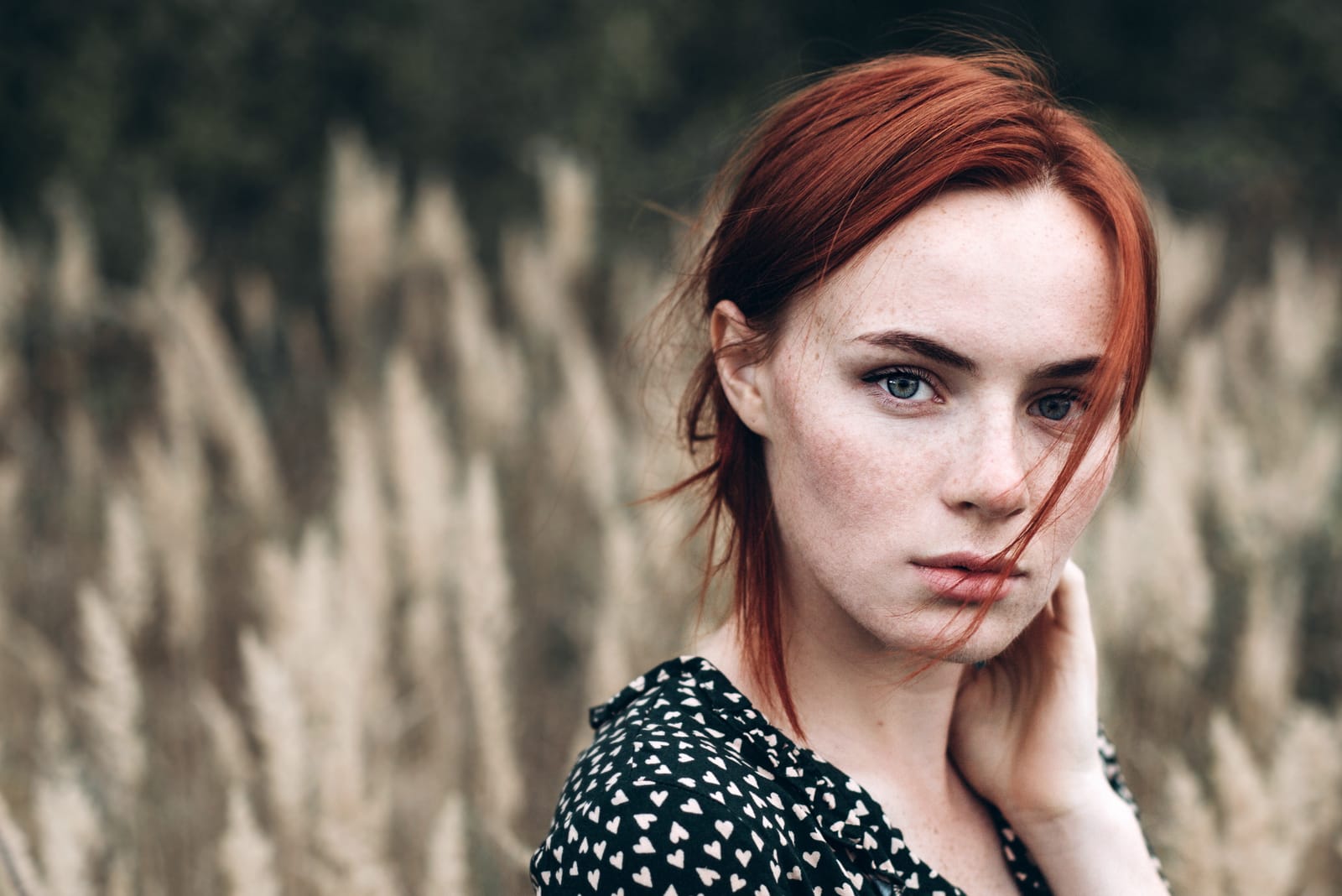 a sad red-haired girl stands in a field of wheat