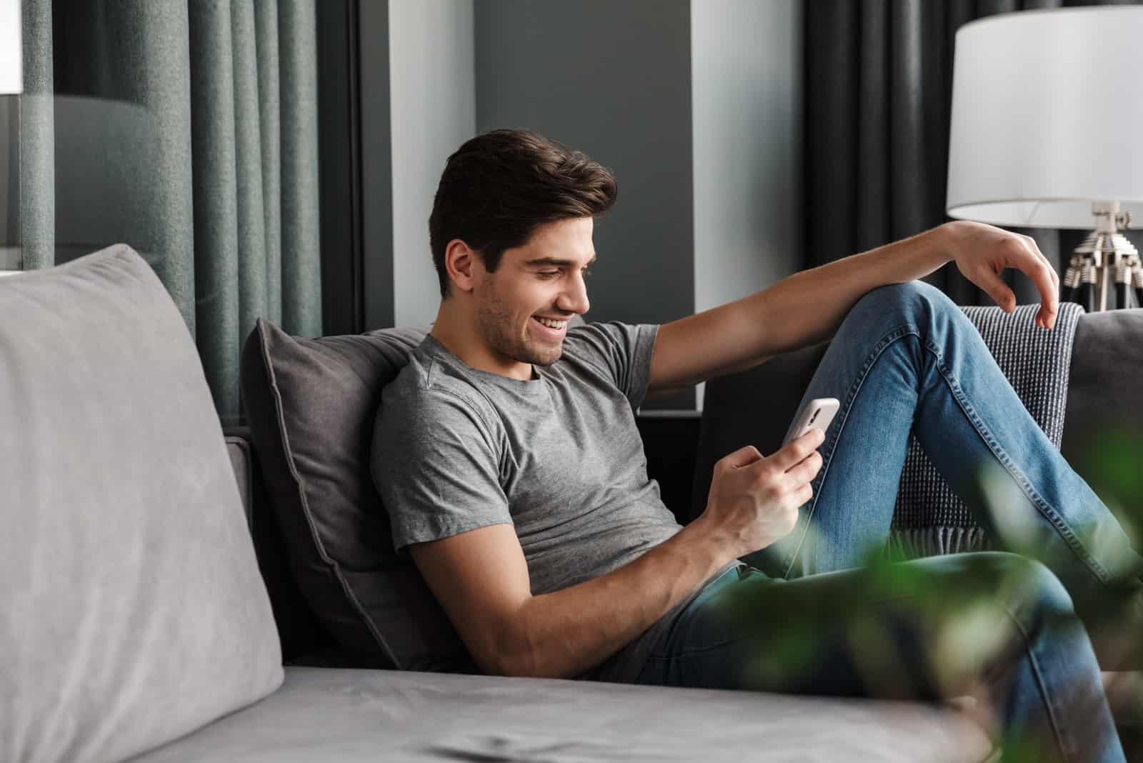un uomo sorridente siede sul divano e digita al telefono