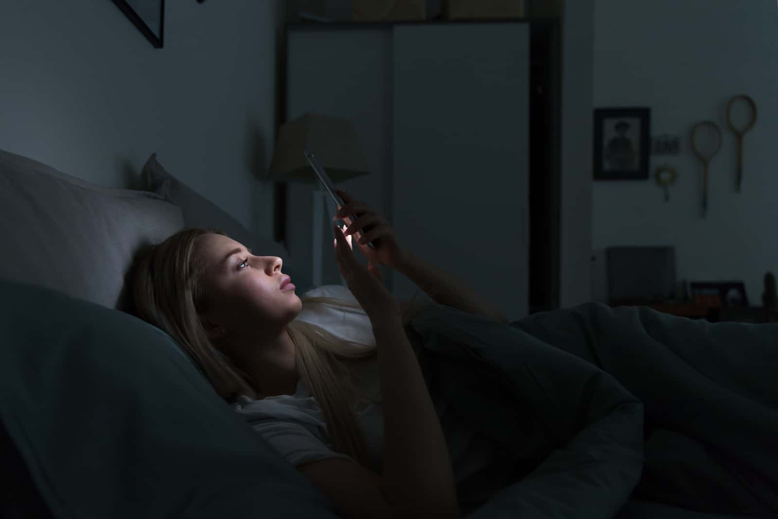 a smiling woman lies in bed and keys on the phone