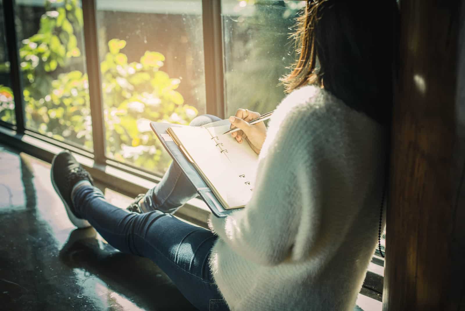 a woman sitting by the window writes
