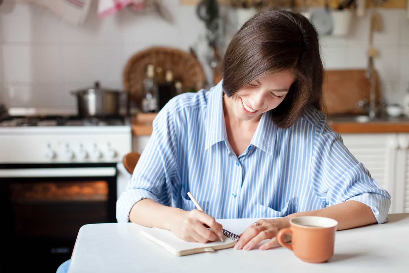 a woman with long black hair sitting by the coffee and writing