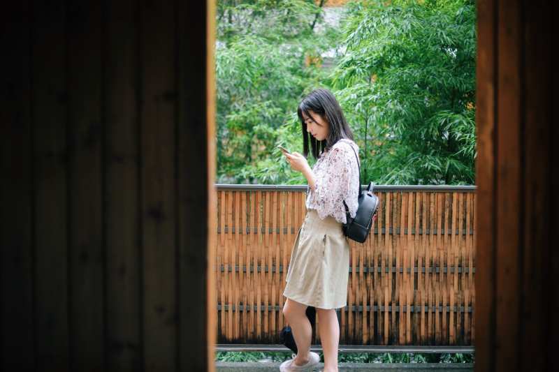 Ragazza asiatica che scrive un messaggio sul suo telefono mentre cammina nella natura