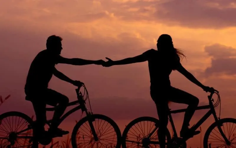 Bicycle couple silhouettes holding hands in sunset