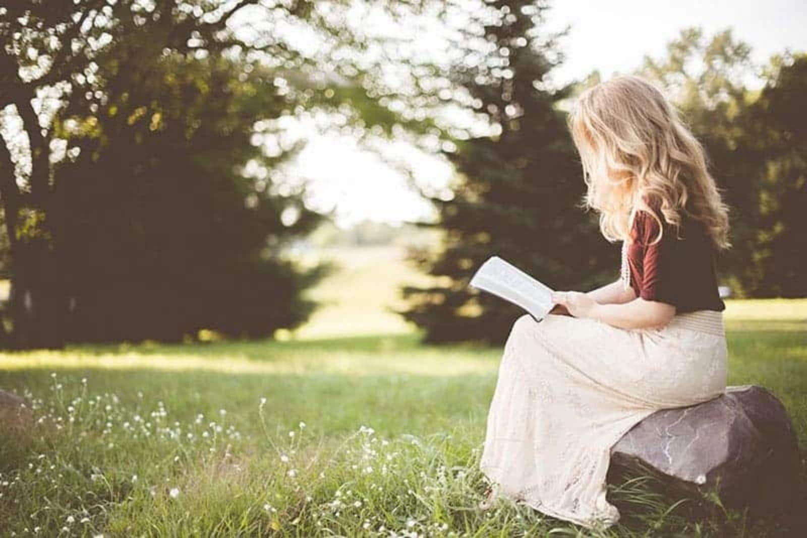 mujer rubia leyendo un libro en la naturaleza