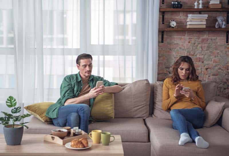 pareja aburrida sentada en el salón y mirando sus smartphones