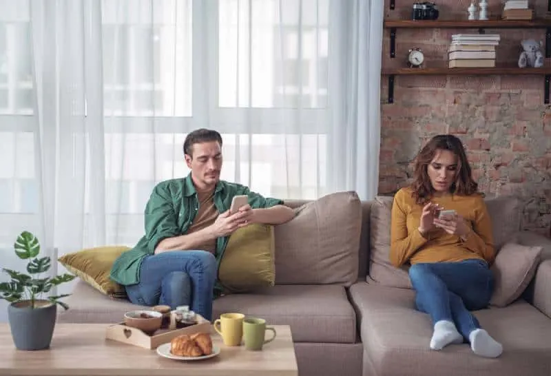 bored couple sitting in living room and looking at their smartphones