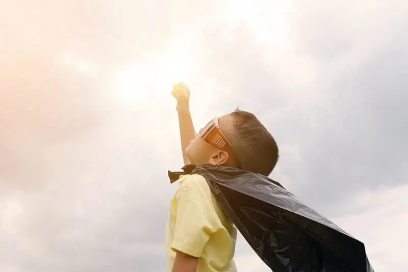 boy playing superhero using black plastic bag as cape