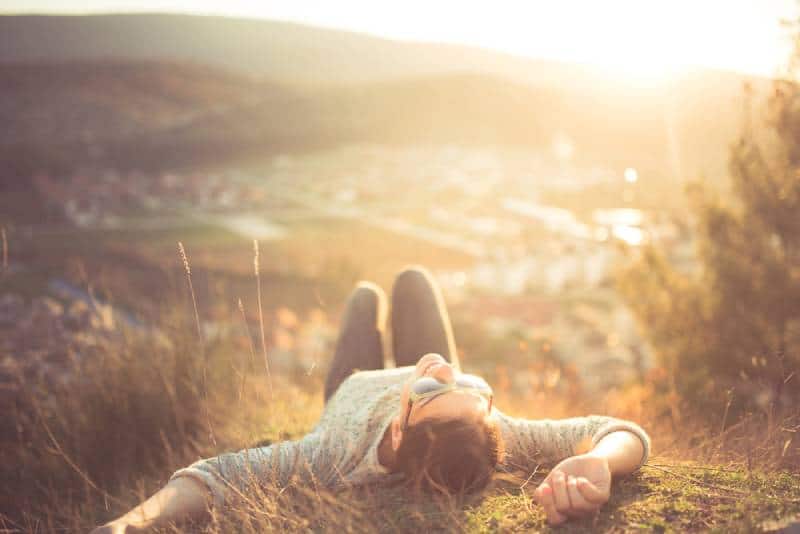 carefree woman lying on grass on top of mountain