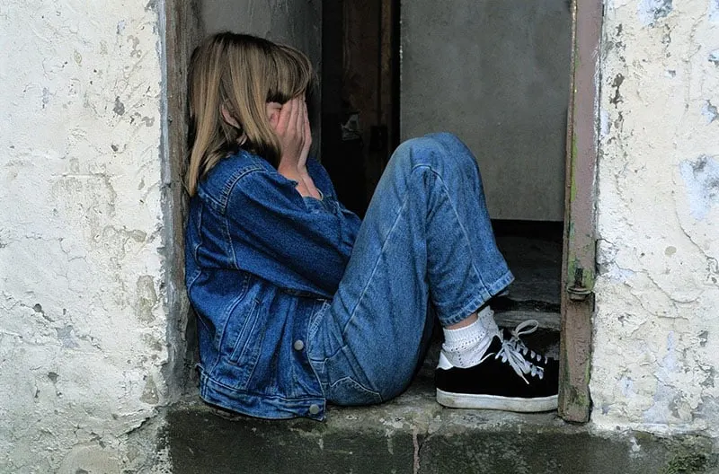 child crying in the doorway wearing denim covering her face