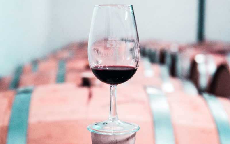 Bicchiere da vino trasparente su una botte con altre botti sullo sfondo