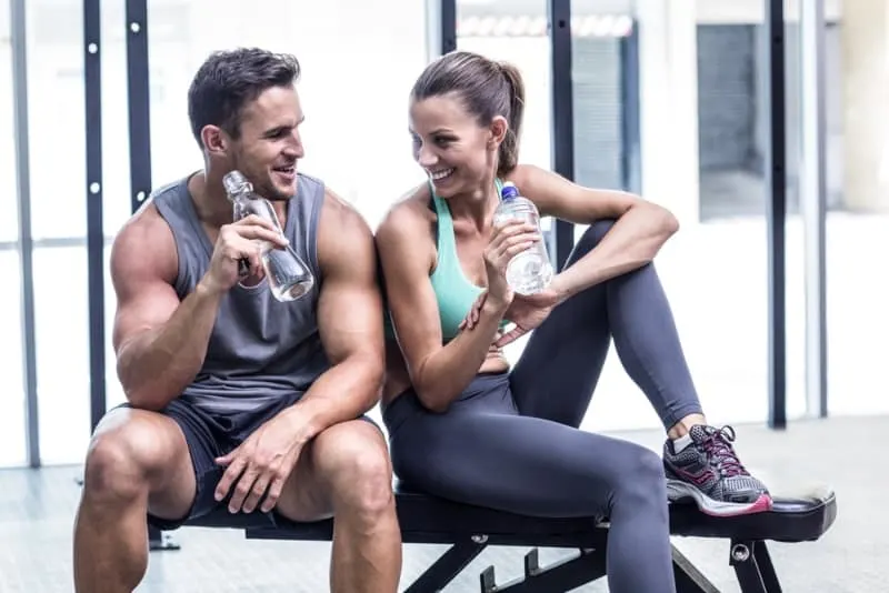 couple drinking water and sitting at gym