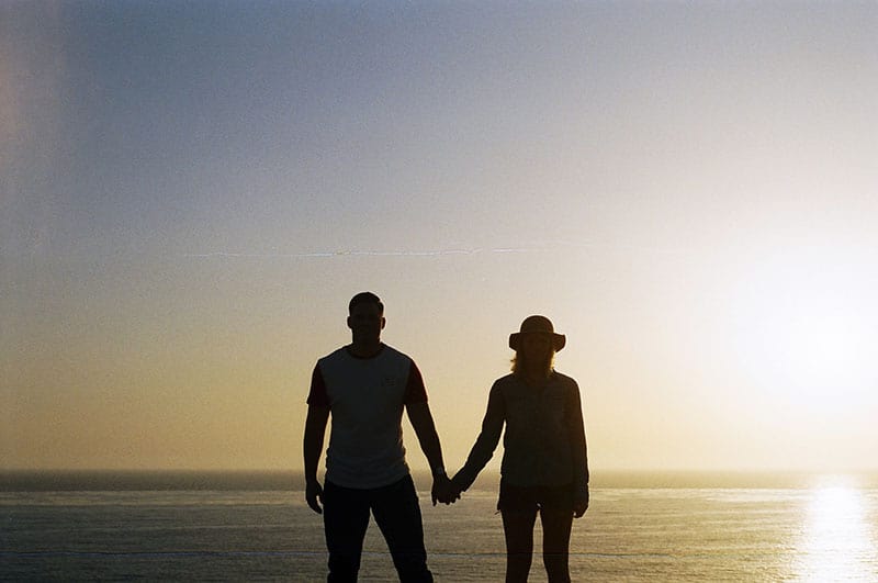 couple holding their hands standing in front of the sea