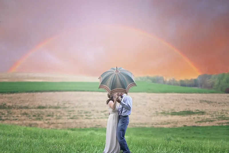 couple holding umbrella while kissing under the rainbow
