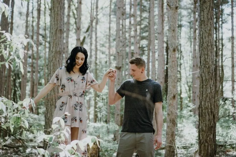 man holding woman's hand in forest