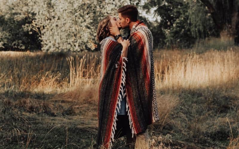 Couple kissing in the forest standing under a blanket