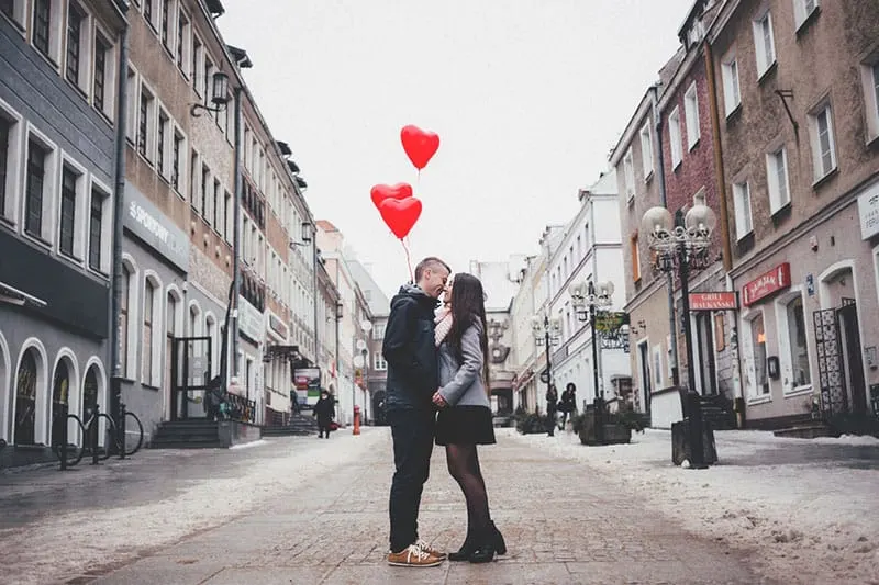 couple kissing in the street with red heart balloons