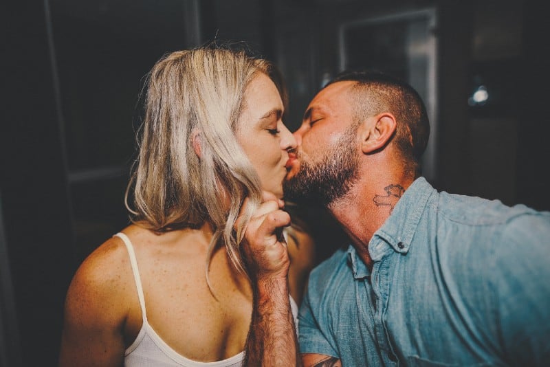 man in blue shirt kissing woman in white top