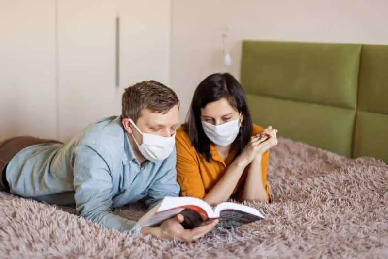 couple lying on bed with protective mask during self-quarantine