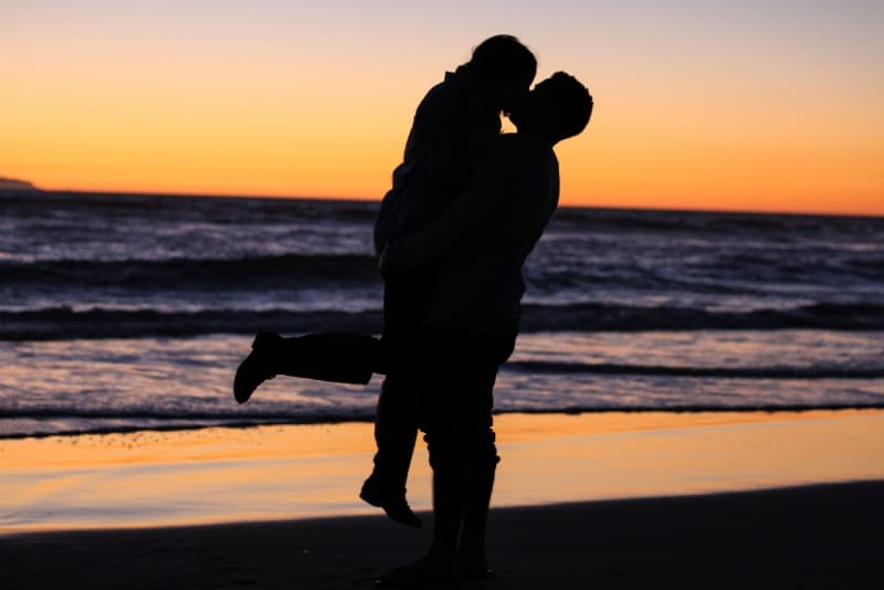 Donna e uomo che si baciano vicino al mare durante l'ora d'oro