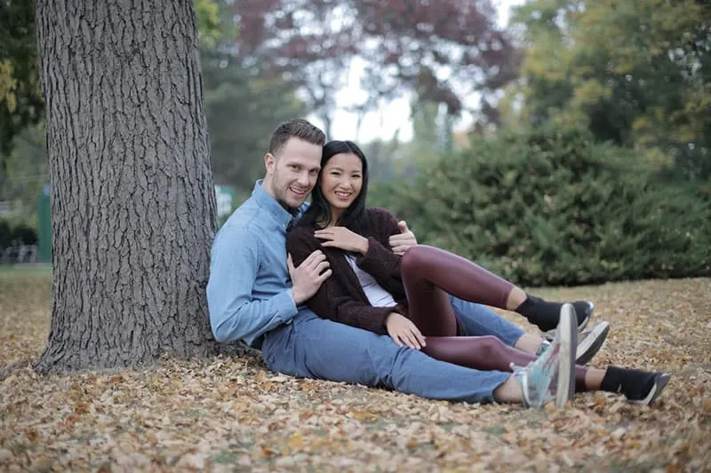 couple cuddling while sitting beside a tree