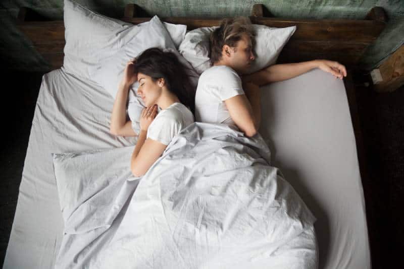 couple sleeping on bed with their backs to each other in bedroom