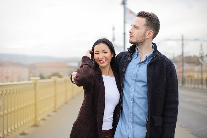 couple standing on sidewalk with man's arms around woman's shoulder