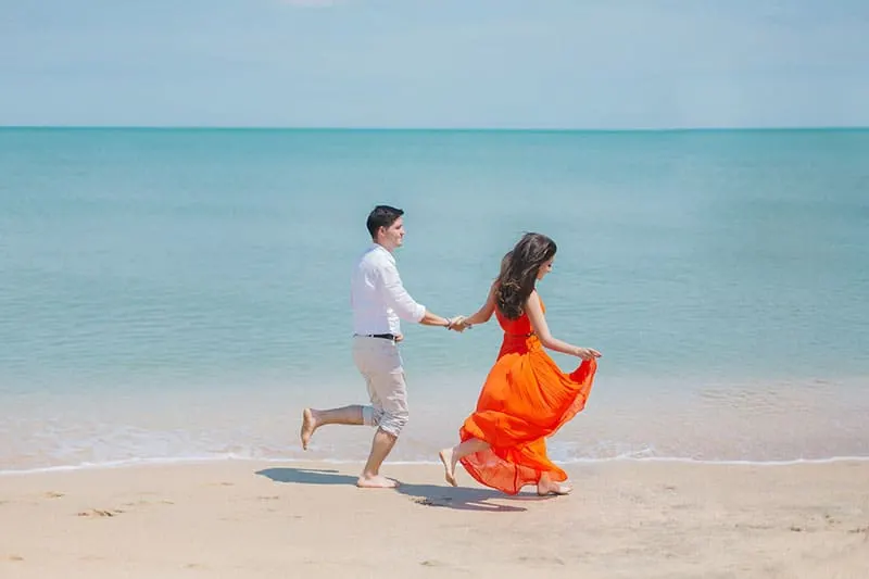 couple walking along the shore with girls orange dress swayed