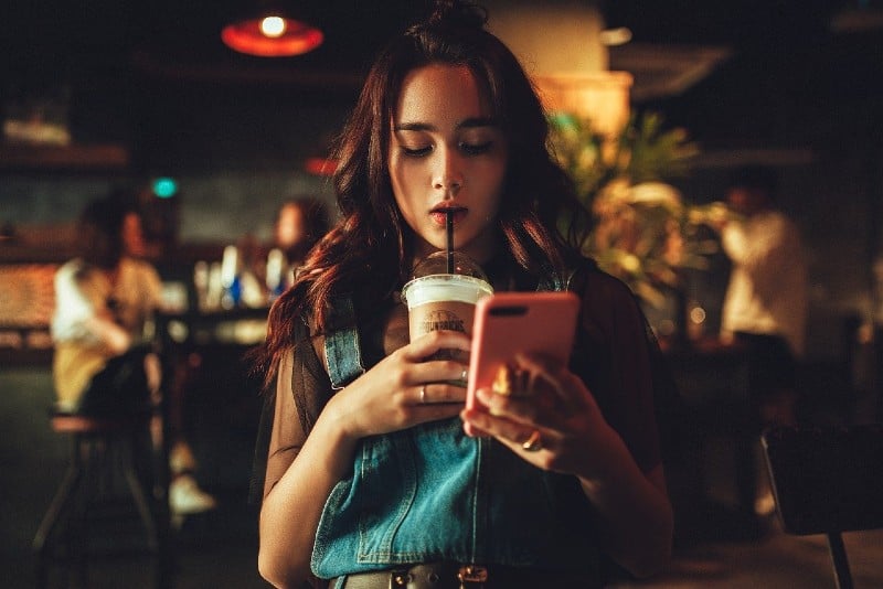 Jovem rapariga a beber café e a utilizar o iphone