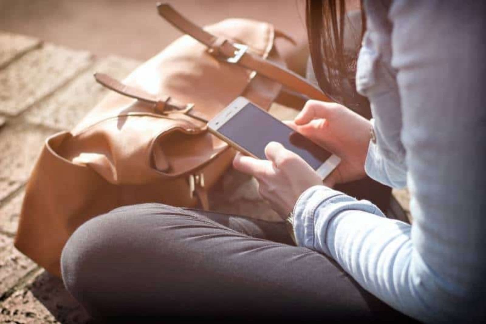 chica sentada sobre ladrillos y tecleando un sms