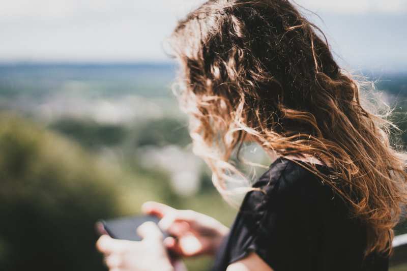 Rapariga com cabelo comprido a enviar mensagens de texto num fundo natural desfocado 