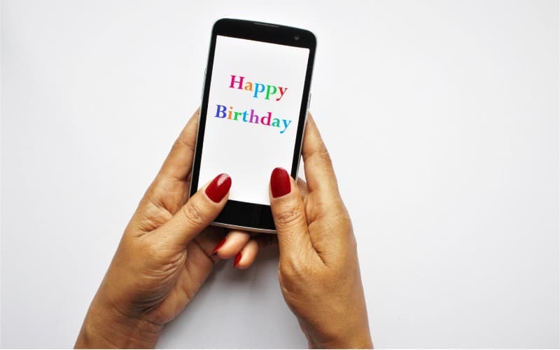 la mano de una mujer en un teléfono inteligente con colorido mensaje de feliz cumpleaños en la pantalla