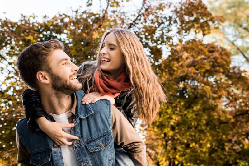 casal feliz a sorrir e a andar às cavalitas na natureza