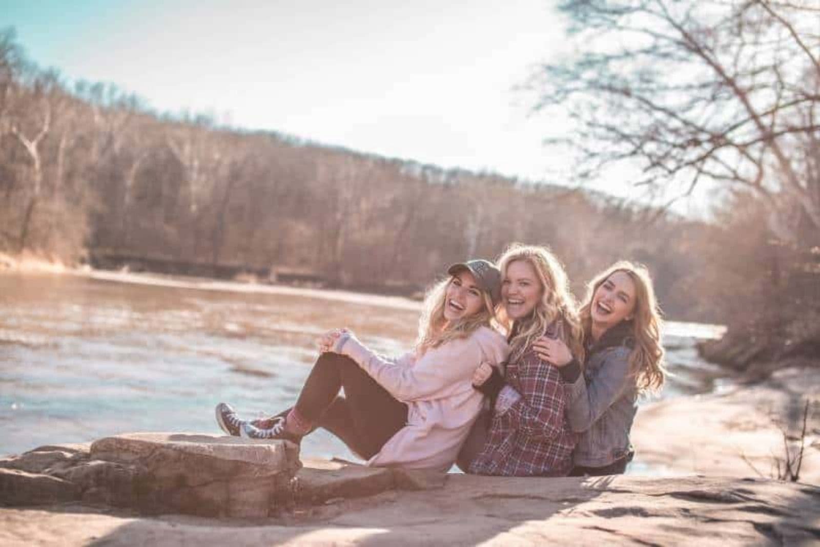 happy female friends sitting by the lake