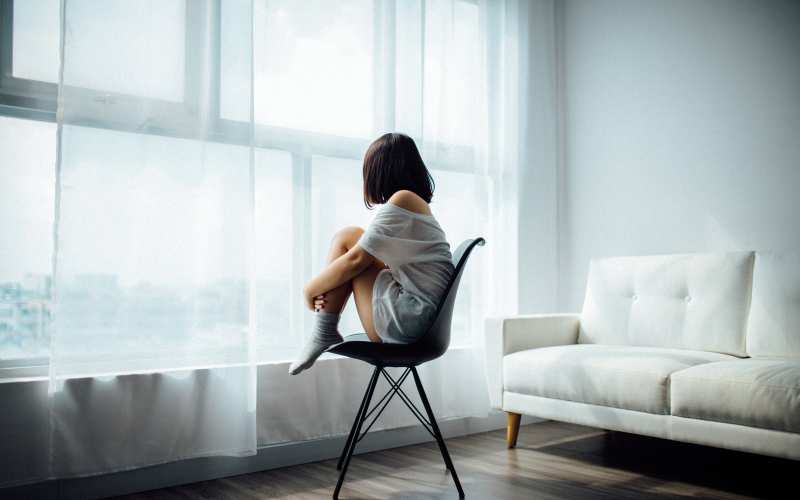 Lonely girl sitting on a chair by the window 