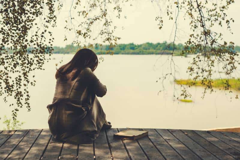 lonely girl sitting on wood at lake