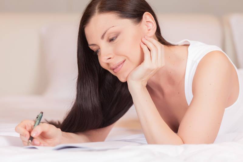 donna sdraiata sul letto che scrive su un foglio