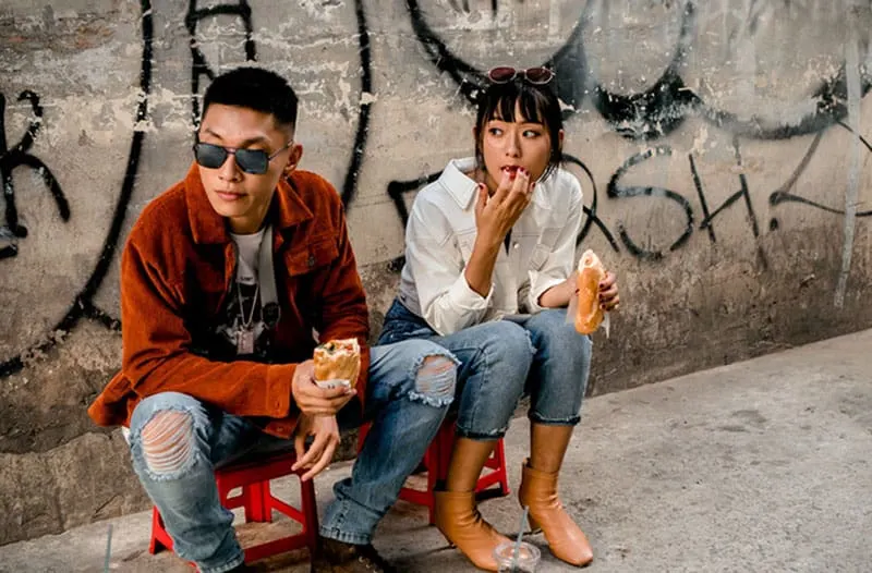 man and woman eating on a sidewalk with vandals on walls sitting on small chairs
