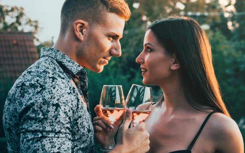 Homem e mulher sensuais frente a frente, muito próximos, com copos de vinho nas mãos