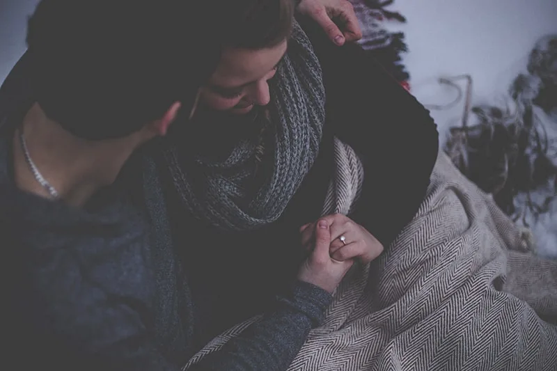 man and woman holding hands while covered with gray blanket