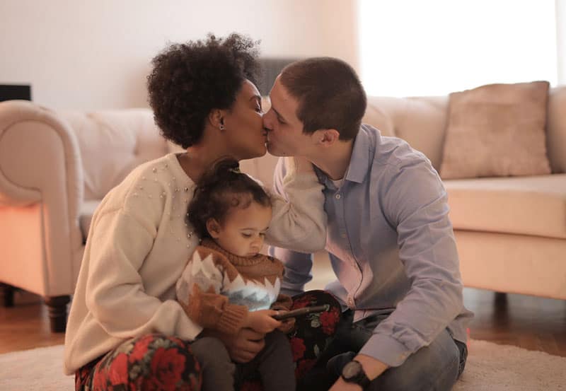 hombre y mujer besandose y niño mirando un gadget