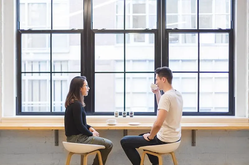 man and woman sat on high chairs on coffee break near the windows