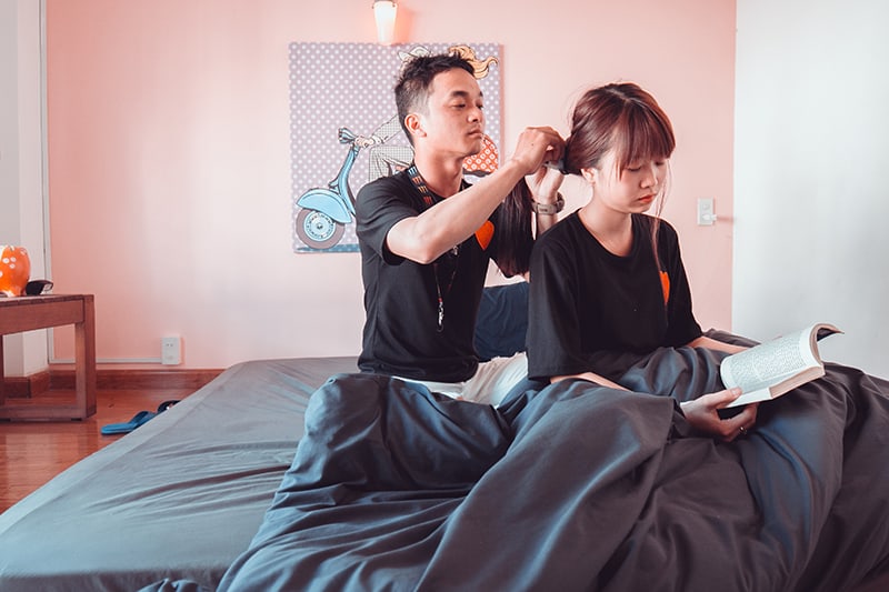 man and woman sitting on bad while man fixing woman's ponytail