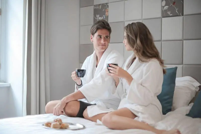 man and woman sitting on bed having breakfast