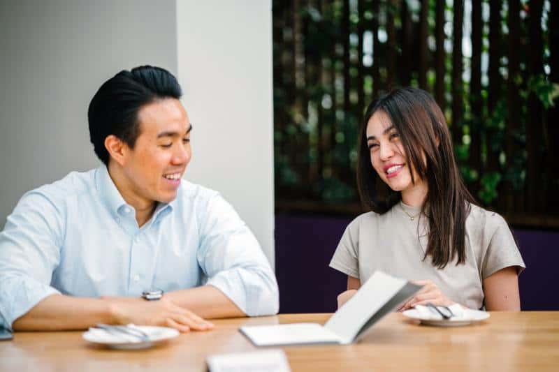 Smiling man and woman sitting on chairs in front of desk and talking