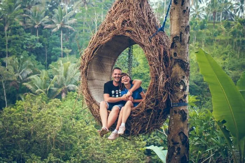 Happy man and woman couple sitting on hanging chair by a tree